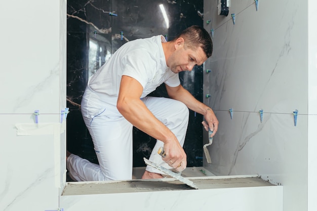 Trabalhador profissional masculino monta ladrilhos de cerâmica na casa de banho