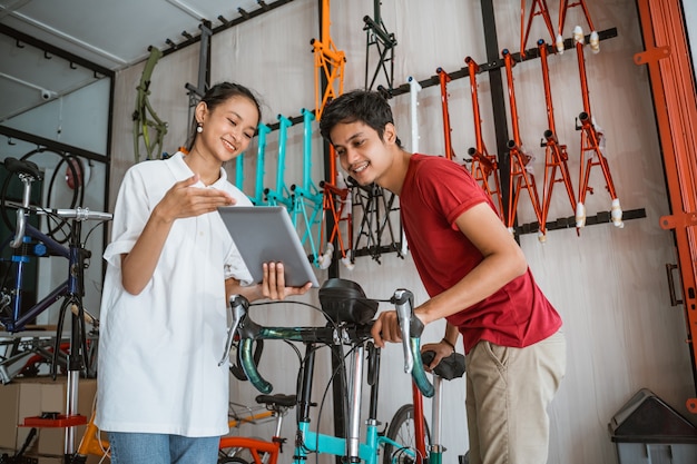 Trabalhador que atende um cliente usando um tablet digital enquanto faz compras na loja de bicicletas