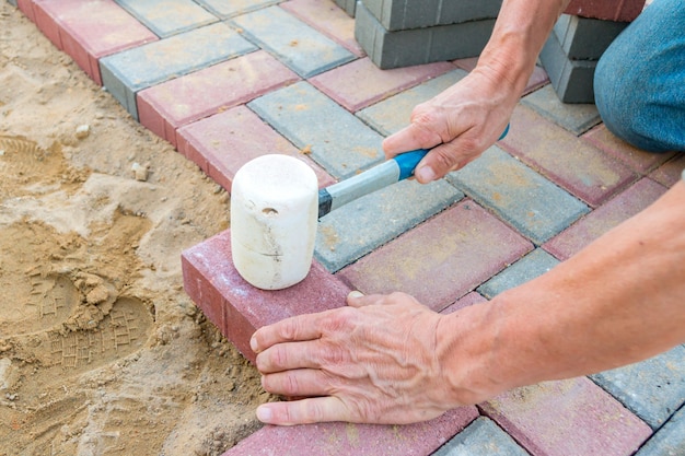 Trabalhador que coloca blocos de pavimentação concretos vermelhos e cinzentos. Pavimentação de estradas, construção.