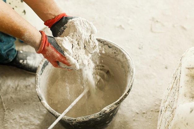 Trabalhador que mistura gesso com água para rebocar paredes construção de casa e conceito de renovação de casa feche o balde com mistura de estuque e mãos de faz-tudo