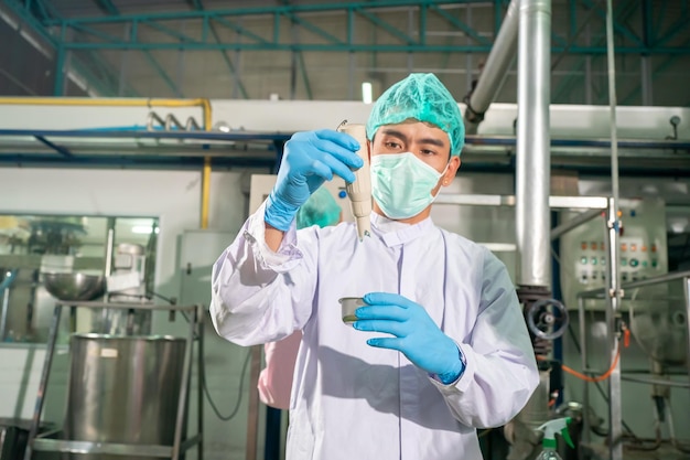 Trabalhador que trabalha na fábrica de bebidas na correia transportadora com copo de suco de frutas engarrafado na linha de produção