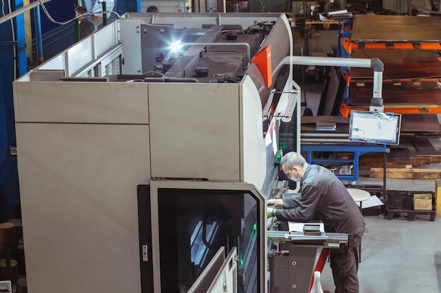 Trabalhador segura uma peça em uma máquina de dobra CNC