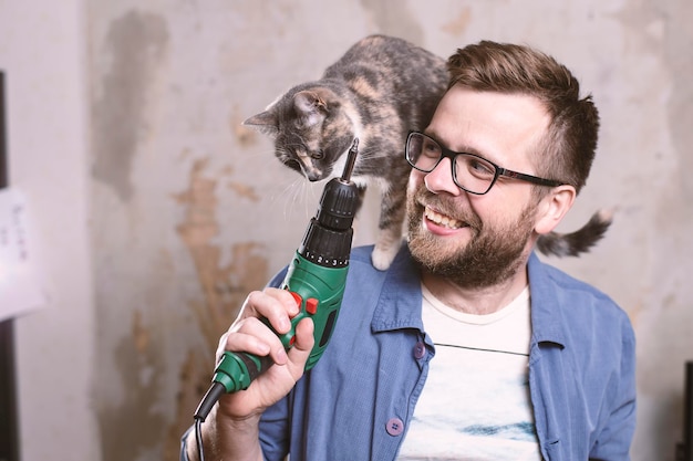 Trabalhador sorridente feliz com furadeira elétrica na mão e um gato no ombro