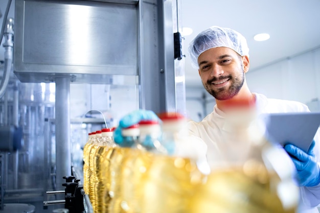 Trabalhador tecnólogo em jaleco branco e rede de cabelo controlando na fábrica de engarrafamento de alimentos