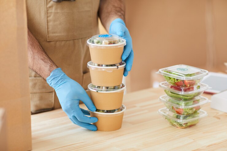 Foto trabalhador usando luvas de proteção, embalando com segurança os pedidos na mesa de madeira em um serviço de entrega de comida