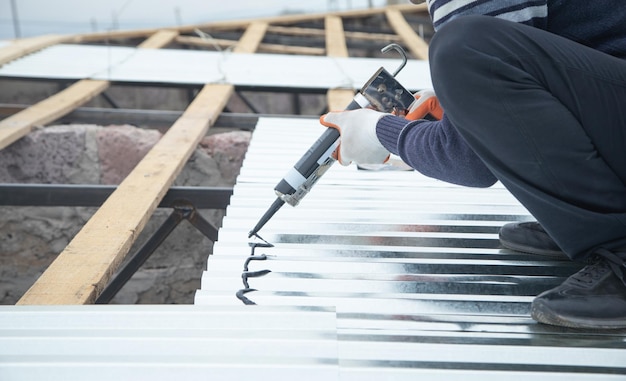 Trabalhador usando pistola de cola com adesivo para fixar o aço metálico no telhado