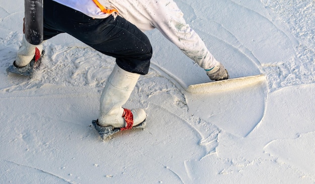 Trabalhador usando sapatos pontiagudos, alisando gesso de piscina molhada com espátula