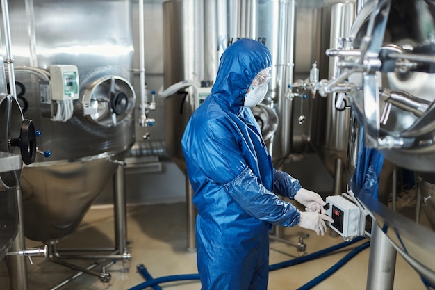 Trabalhador vestindo traje de proteção pressionando botões no equipamento na oficina da fábrica