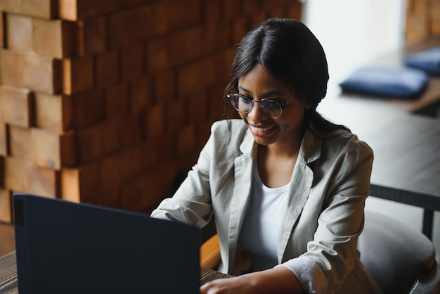 Trabalhadora afro-americana feliz usando o estudo de trabalho do laptop no computador no escritório do sotão ou café sorrindo aluna de raça mista freelancer usando aplicativo de pc namoro se comunicando on-line assistindo webinar