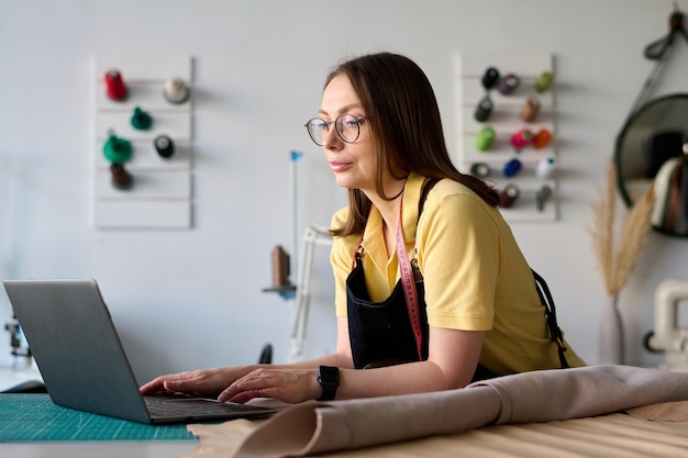 Trabalhadora de couro feminina madura sentada à mesa na frente do laptop