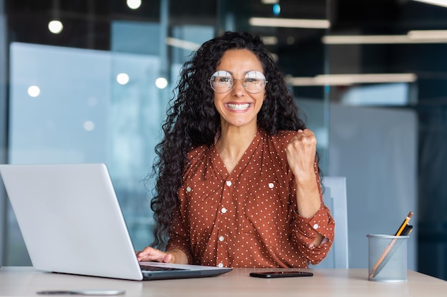 Foto trabalhadora de escritório hispânica bem-sucedida do retrato com cabelo encaracolado sorrindo e olhando para