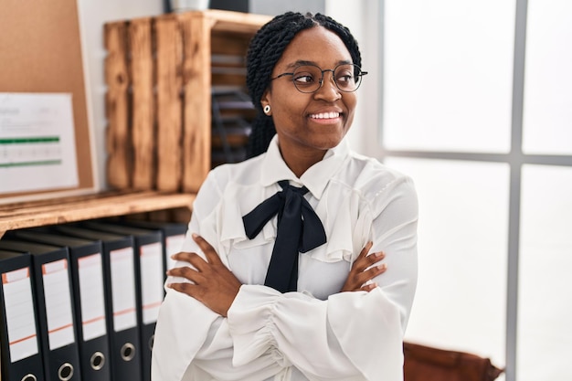 Trabalhadora de negócios de mulher afro-americana sorrindo confiante em pé com gesto de braços cruzados no escritório