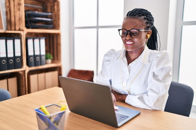 Trabalhadora de negócios de mulher afro-americana usando laptop e fones de ouvido no escritório