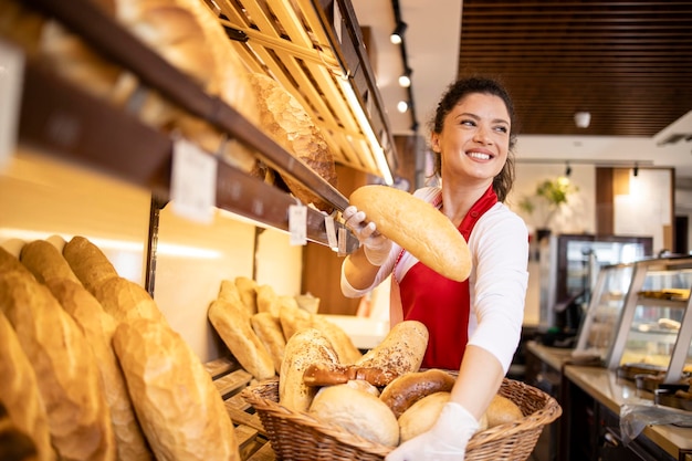 Foto trabalhadora de padaria de uniforme vendendo pão para o cliente na padaria