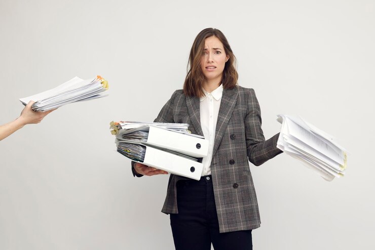 Foto trabalhadora estressada e mulher de negócios segurando uma pilha de papelada enquanto tem mais trabalho a fazer, parecendo frustrada na câmera, isolada em fundo branco.
