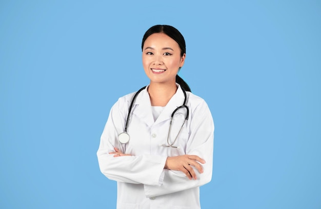 Trabalhadora médica sorrindo médica asiática de uniforme em pé com braços cruzados