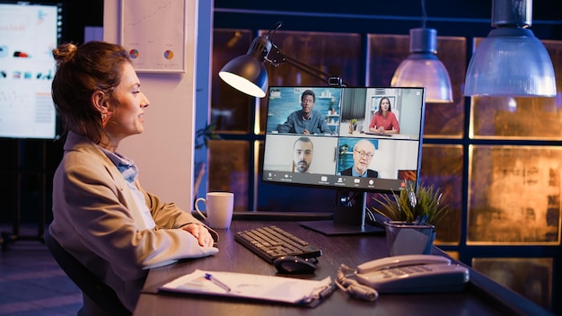 Trabalhadora participando de reunião corporativa remota usando teleconferência e webcam no pc, conversando com colegas de trabalho. Jovem adulto conversando em conferência de videochamada online à noite. Tiro portátil.