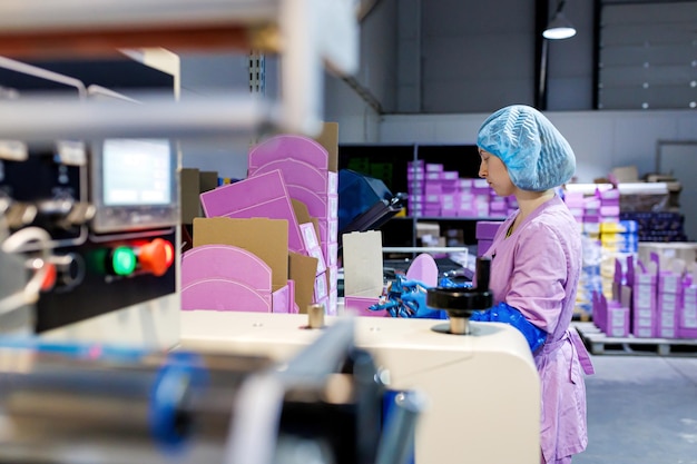 Trabalhadora profissional em uniforme e luvas protetoras embaladas bombons de chocolate em caixas na linha de produção na fábrica