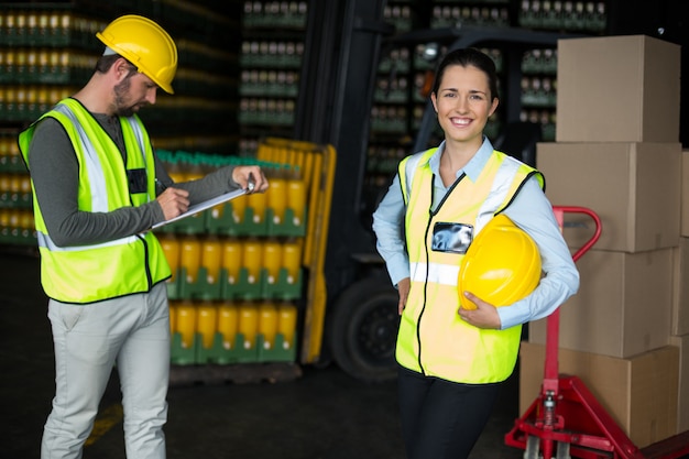 Trabalhadora, sorrindo para a câmera enquanto colega de trabalho escrevendo na área de transferência