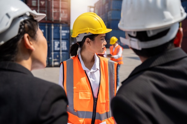 Trabalhadora trabalhando com Foreman, segurando um capacete amarelo para controlar o carregamento e verificar a qualidade dos contêineres do navio de carga para importação e exportação no estaleiro ou porto