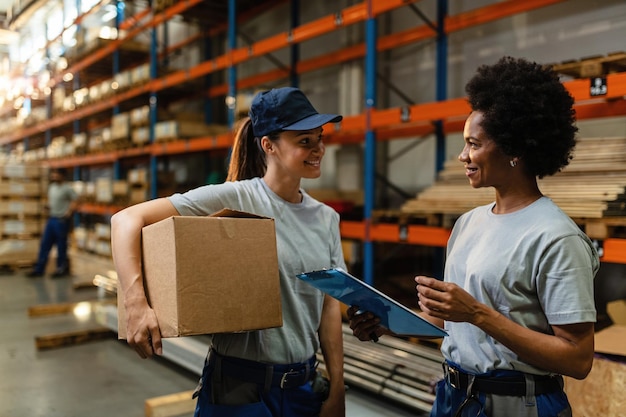 Trabalhadoras de armazém felizes conversando umas com as outras enquanto preparam o envio para distribuição em armazém industrial