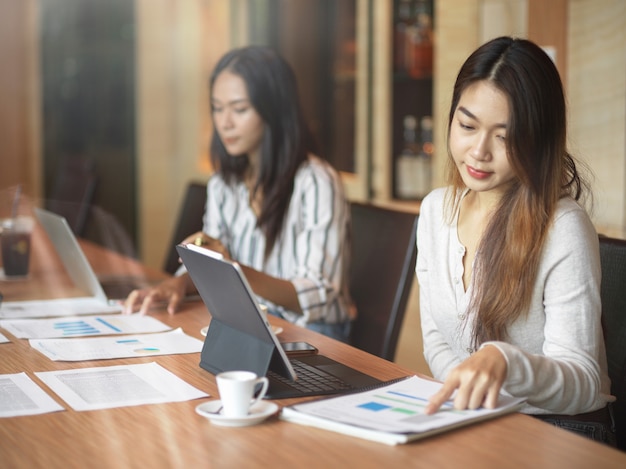 Trabalhadoras de negócios asiáticos concentrando seu trabalho na sala de escritório com relatório financeiro, laptop e xícara de café