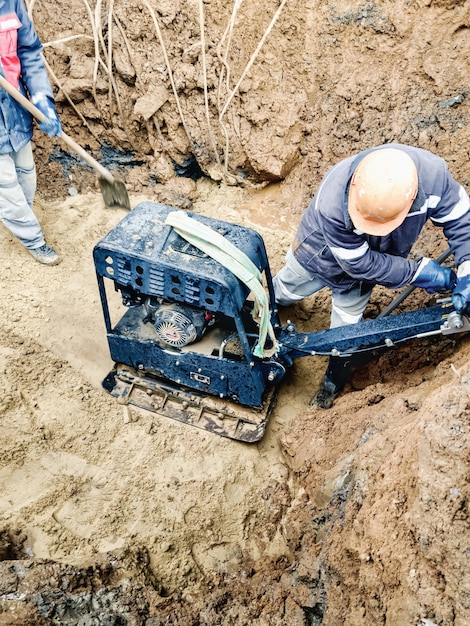 Trabalhadores compactam o solo com máquina de socaria de ferramentas de trabalho especial ou placa vibratória preparação da fundação