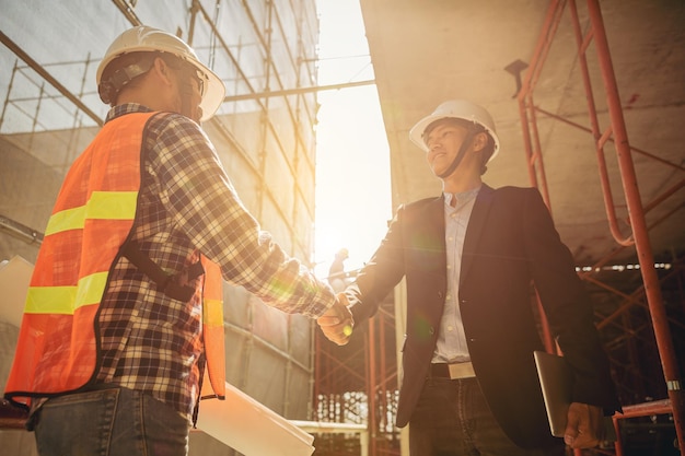 Trabalhadores da construção civil de arquiteto e engenheiro apertando as mãos enquanto trabalhavam no canteiro de obras ao ar livre