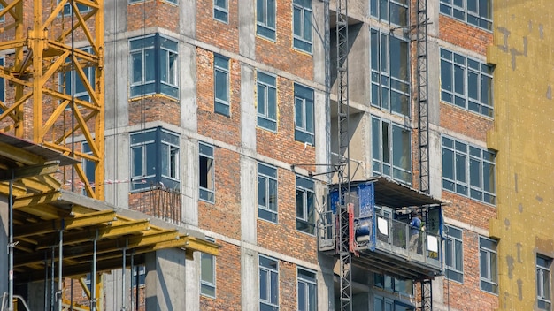 Trabalhadores da construção civil descendo na fachada do elevador com janelas