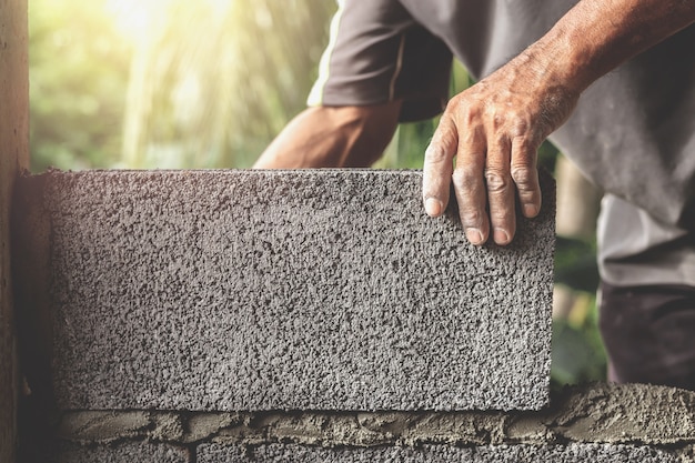 Trabalhadores da construção civil estão construindo paredes de cimento com blocos de tijolos.