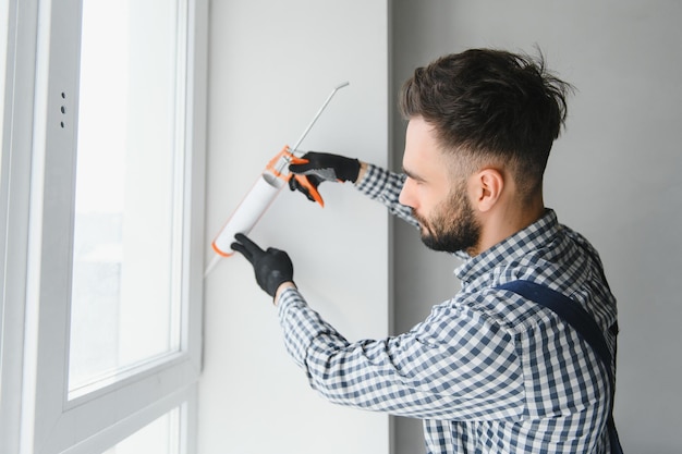 Trabalhadores da construção civil instalam janelas de portas e usam silicone e selante