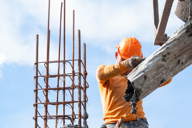 Trabalhadores da construção civil no local da construção despejando concreto na forma, homem trabalhando em altura com céu azul no local da construção