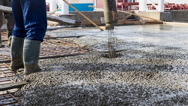 Trabalhadores de construtores despejam piso de concreto em oficina industrial. Pernas em botas em concreto. Submissão de concreto para despejar o piso. Obras de concreto monolíticas.