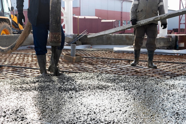 Trabalhadores de construtores despejam piso de concreto em oficina industrial. Pernas em botas em concreto. Submissão de concreto para despejar o piso. Obras de concreto monolíticas.