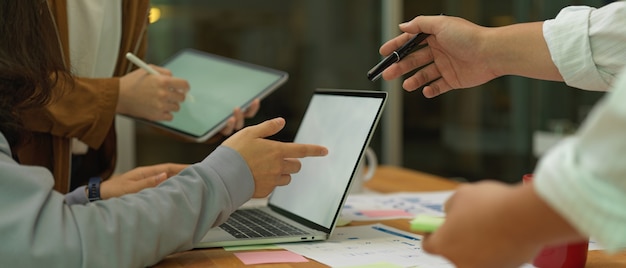 Trabalhadores de escritório trabalhando juntos com simulações de dispositivos digitais e papelada na sala de reuniões