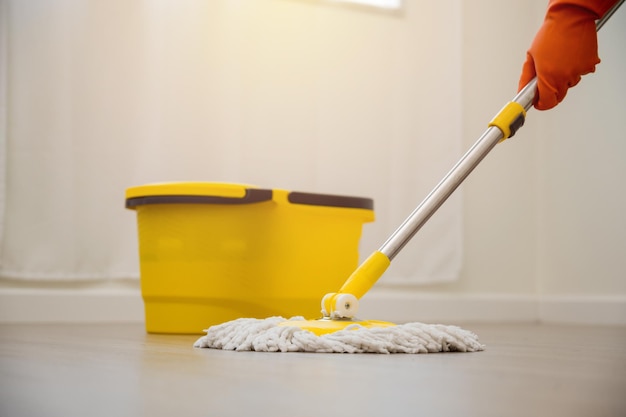 Trabalhadores de limpeza passando o esfregão na área molhada. houve derramamento de água no piso de madeira da sala. conceito de serviço de limpeza em casa.