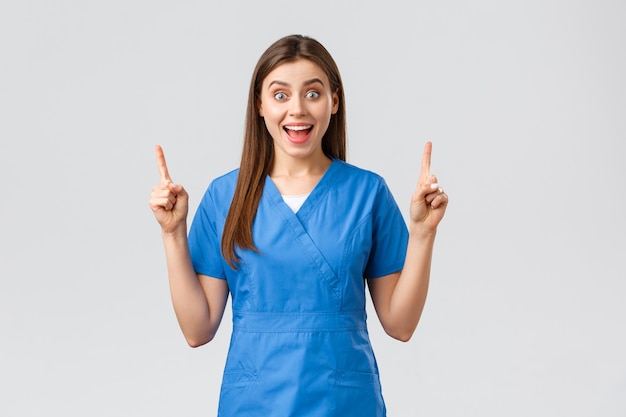 Trabalhadores de saúde, previnem o conceito de vírus, seguro e medicina. Enfermeira ou médico animado e feliz em uniforme azul sorrindo com boas notícias, apontando o dedo para cima, mostrando aos pacientes ótimas notícias