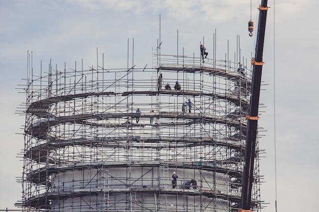 Trabalhadores do sexo masculino da construção tanque de óleo instalando andaimes e guindaste na refinaria do local