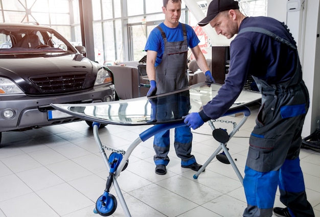 Trabalhadores especiais de automóveis substituindo pára-brisas ou pára-brisas de um carro na garagem da estação de serviço automóvel.