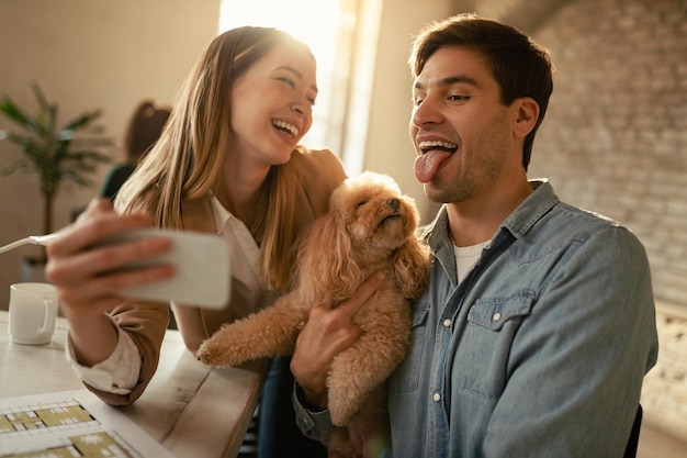 Trabalhadores freelance lúdicos tirando selfie com um poodle e se divertindo no escritório