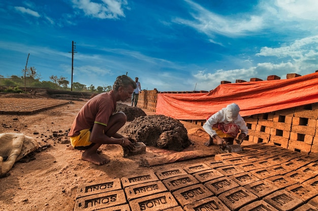 Trabalhadores indianos fazendo tijolos de barro manualmente na fábrica ou no campo.