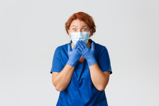Trabalhadores médicos, pandemia de covid-19, conceito de coronavírus. Enfermeira de meia-idade, surpresa e impressionada, médica com máscara facial e luvas de borracha, ofegando olhando com espanto para a câmera.