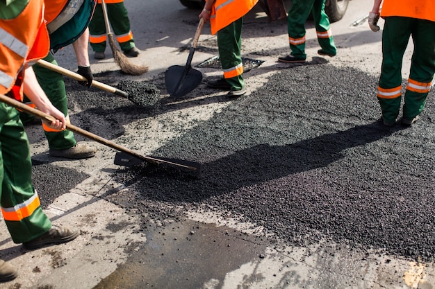 Trabalhadores na máquina pavimentadora de asfaltagem durante obras de reparação de estradas