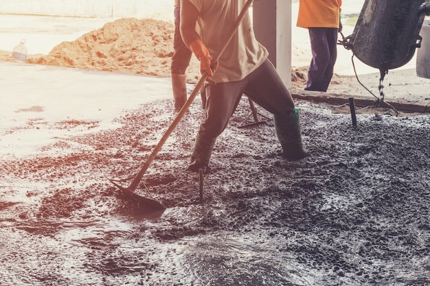 Trabalhadores que espalham mistura de concreto recém-derramado na construção com tom vintage.