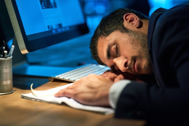 Trabalhando até a morte Foto de um jovem empresário exausto dormindo em sua mesa durante uma noite de trabalho
