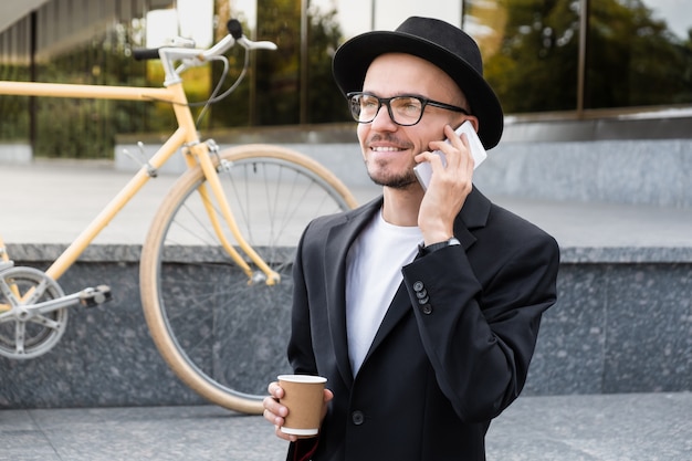 Trabalhando com tecnologia fora do conceito de escritório. Retrato de jovem em terno casual falando ao telefone em área urbana