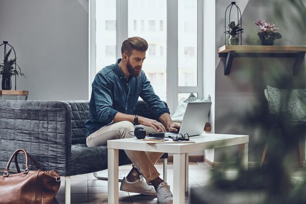 Trabalhando duro para alcançar o sucesso. Homem jovem pensativo e moderno usando o computador enquanto está sentado em seu local de trabalho