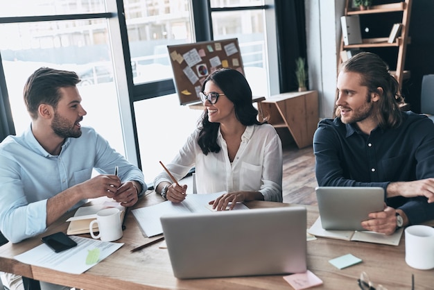 Trabalhando em equipe. Grupo de jovens modernos em roupas casuais inteligentes trabalhando juntos e sorrindo