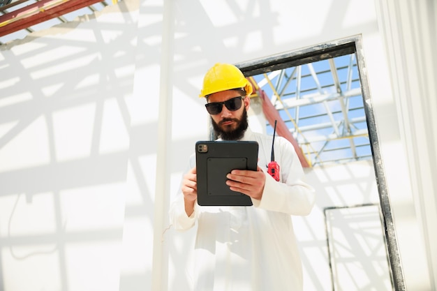 Trabalhando em tablet e walkie talkie Homem árabe Engenheiro civil de construção usa computador tablet digital e usando capacete de segurança trabalhando no canteiro de obras