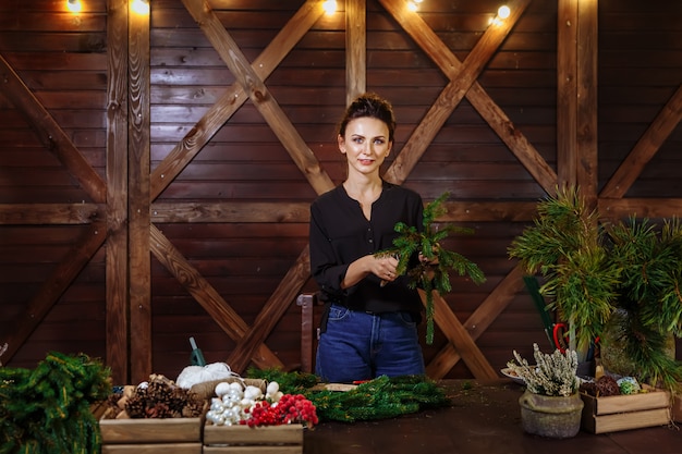 Trabalhando florista mulher com guirlanda de Natal, jovem bonito sorridente desenhador mulher preparando Natal Evergreen Tree Wreath.